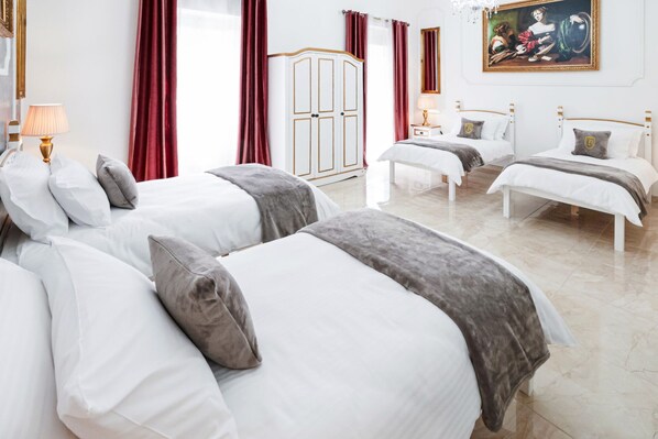 Hotellihuone, jossa on kolme sänkyä, vaatekaappi ja taulu seinällä.