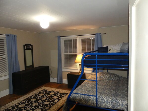 Une chambre à coucher avec un lit superposé, une commode, un miroir et une fenêtre avec des stores.
