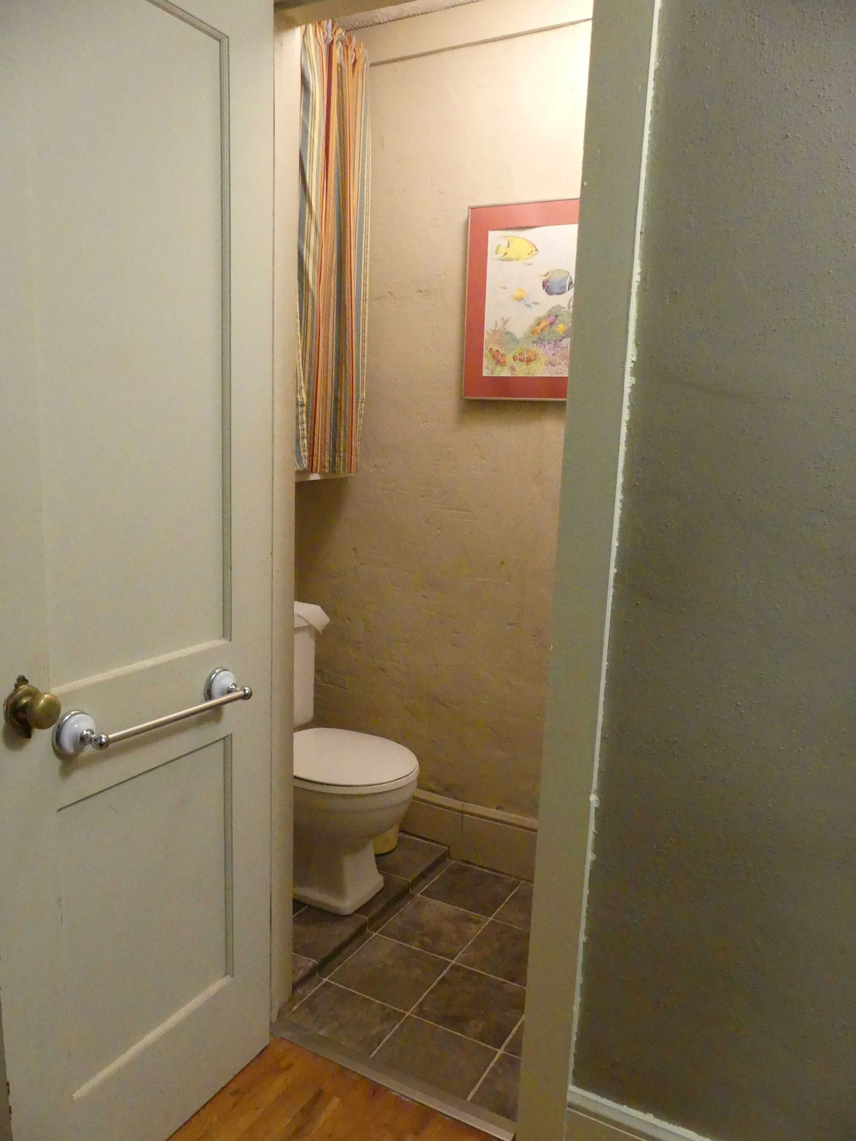 A bathroom with a toilet, a striped shower curtain, and a framed picture on the wall.