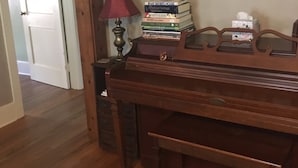 Een houten piano met een bankje, een stapel boeken, een rode lamp en een ingelijst plaatje aan de muur.