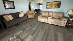 Un salon avec un canapé marron, un canapé en cuir beige et un fauteuil en cuir marron. On aperçoit une table à manger avec des chaises à l'arrière-plan.