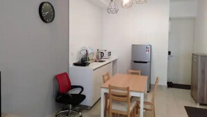 A compact kitchen with a refrigerator, a coffee maker, and a microwave on the counter. There is a dining table with chairs and a red office chair. - Premium Suite Studio KLCC Arte+ (Kuala Lumpur)