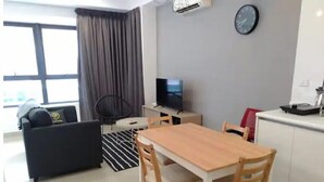 A modern living room with a sofa, a dining table with chairs, a TV, and a clock on the wall. - Premium Suite Studio KLCC Arte+ (Kuala Lumpur)