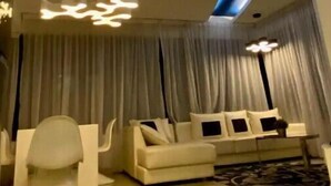 A modern living room with a white sofa, a white armchair, and a coffee table. There is a large window with curtains, and a unique ceiling light fixture. - Signature Premium Suite KLCC Arte+ 2R2B (Kuala Lumpur)