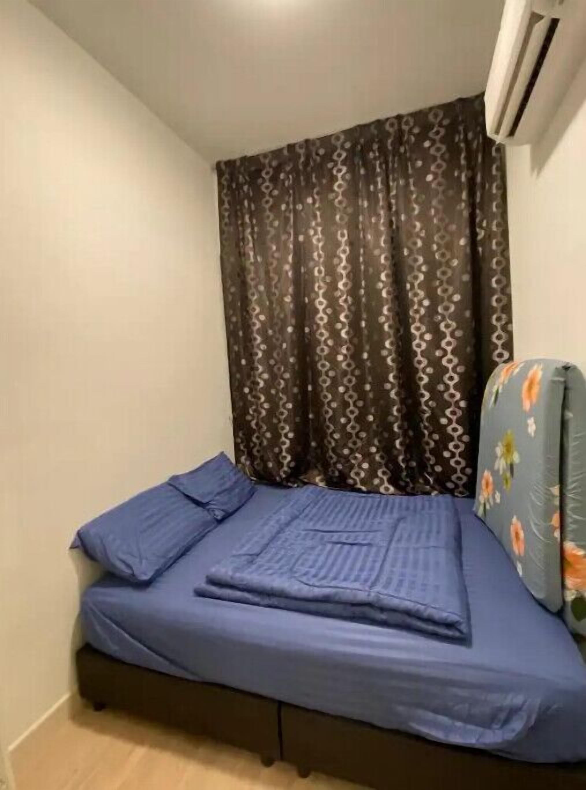 Ein kleines Zimmer mit einem Einzelbett, einem dunklen, gemusterten Vorhang, einer blauen Bettdecke und einem floralen Sessel.