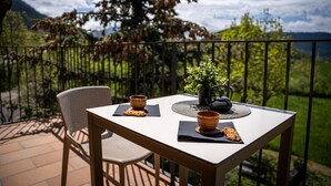A table with two bowls, a teapot, and a plant on a balcony with a view of mountains and greenery. - Hostal Cal Franciscó (Gosol)