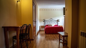 A room with a wooden floor, a bed with a red bedspread, a desk with a chair, and a nightstand. - Hostal Cal Franciscó (Gosol)