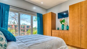 Quarto com uma cama grande, guarda-roupa de madeira, televisão de tela plana e vista para um edifício e árvores pela janela.