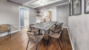 A dining area with a long wooden table and wicker chairs, a kitchen in the background, and a ceiling fan. - 5mins to Kyle Field, 5BR w Private Backyard & Pool (Bryan)