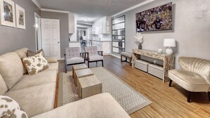A spacious living room with a neutral color palette, featuring a sofa, armchairs, a coffee table, and a TV mounted on the wall. - 5mins to Kyle Field, 5BR w Private Backyard & Pool (Bryan)