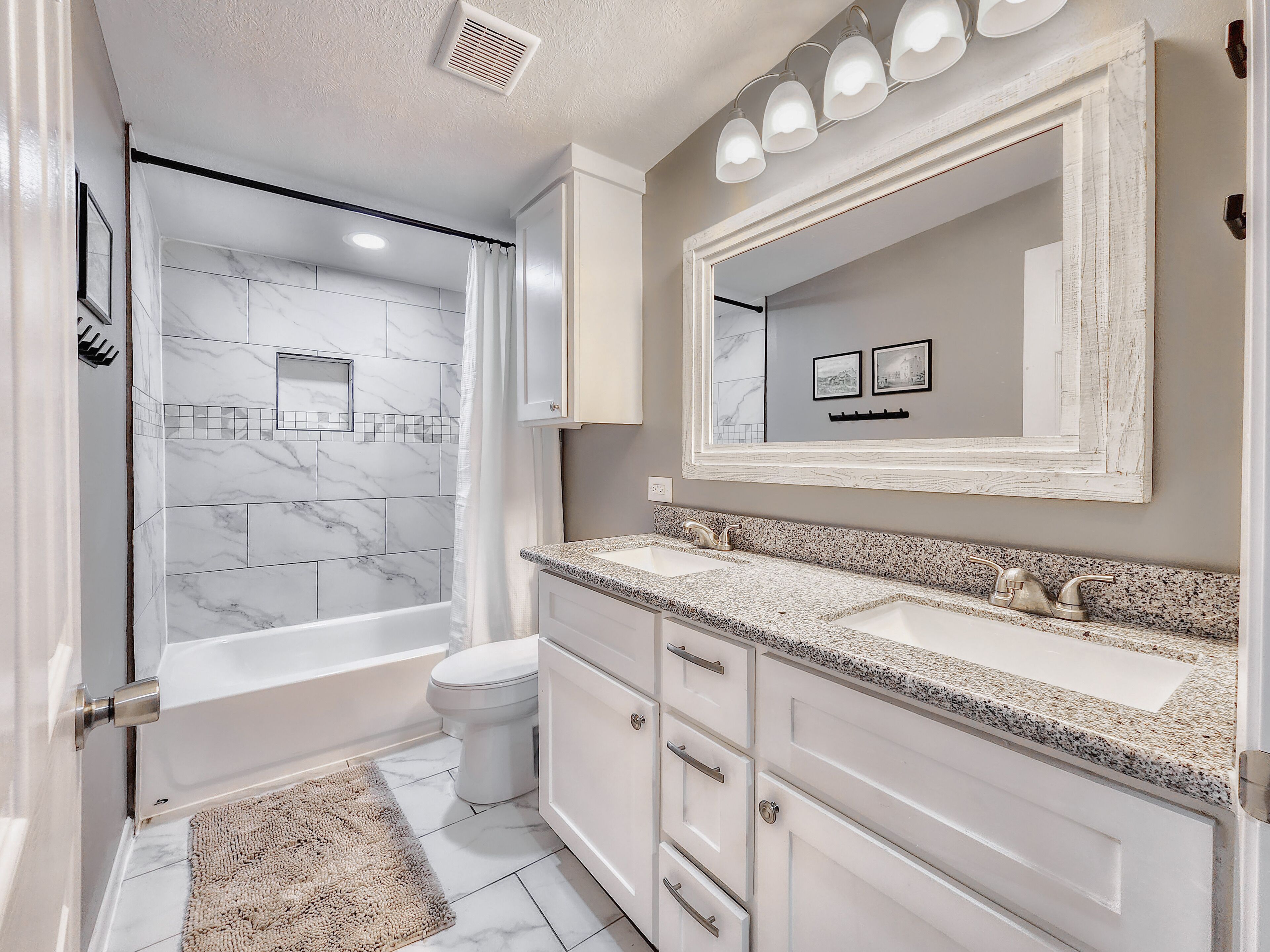 A modern bathroom with a bathtub, toilet, and vanity with a large mirror.