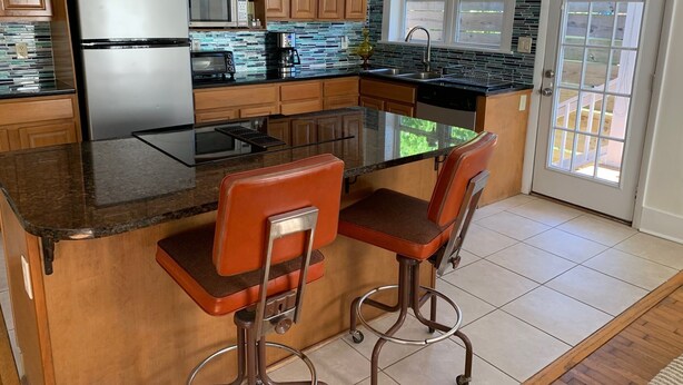 Een keuken met houten kastjes, een roestvrijstalen koelkast, een magnetron, een broodrooster en een groot kookeiland met barkrukken.