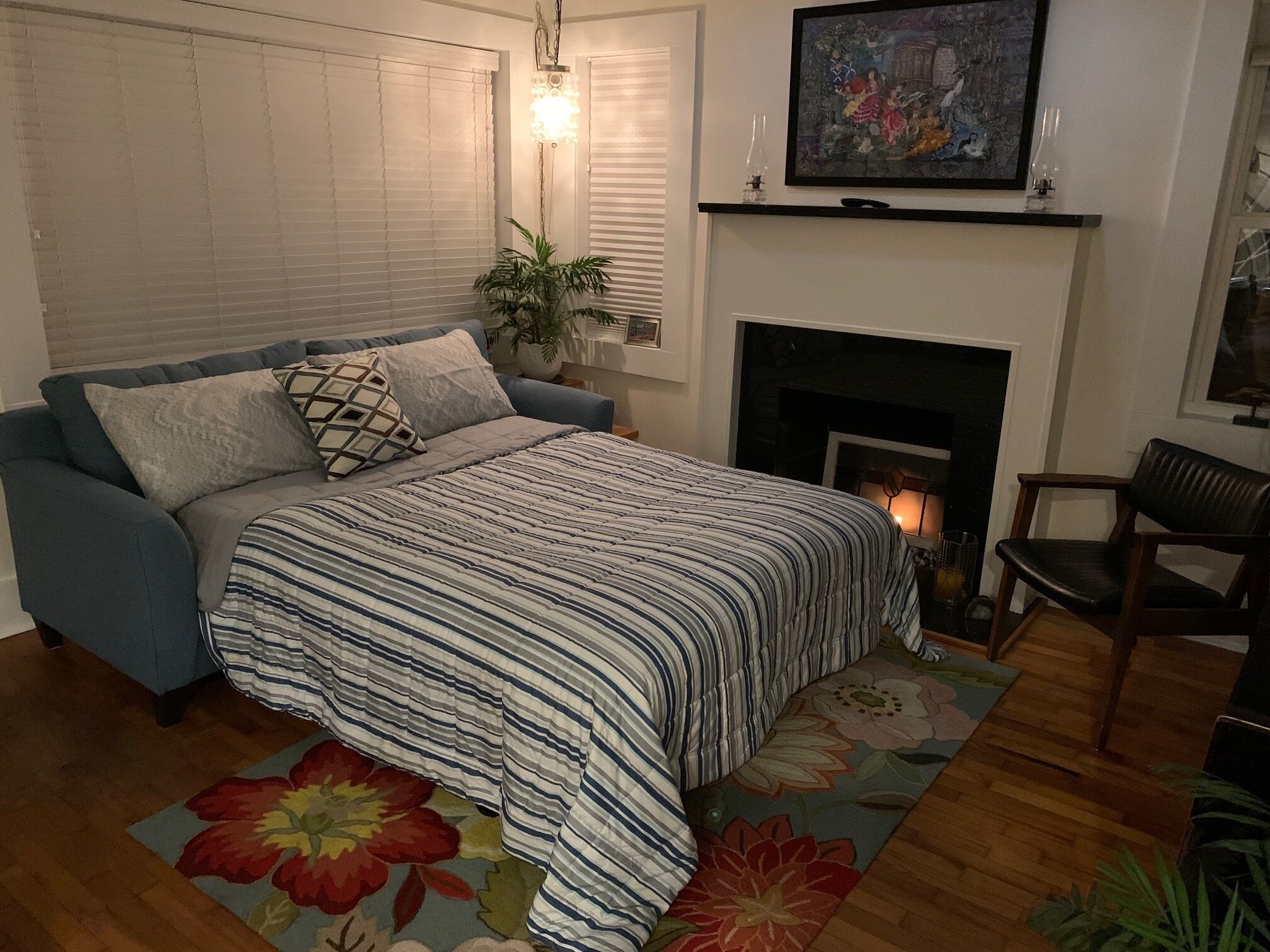 A bedroom with a bed, a blue sofa, a fireplace, and a painting on the wall.