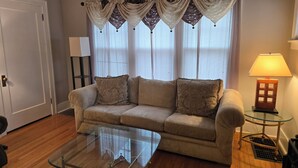 A living room with a beige sofa, a glass coffee table, and a lamp on a side table.