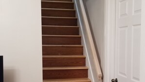 A staircase with wooden steps leading to a landing, a white door, and a patterned armchair.