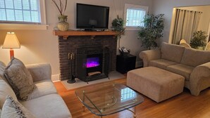 A living room with a fireplace, a sofa, a glass coffee table, and a television.