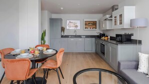 Une cuisine moderne avec des meubles gris, une table à manger avec des chaises orange et un canapé gris.