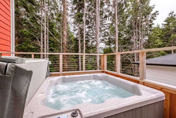A hot tub on a wooden deck with a view of tall trees.