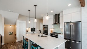 Una cocina moderna con armarios blancos, una isla grande con taburetes de bar, electrodomésticos de acero inoxidable e iluminación colgante.