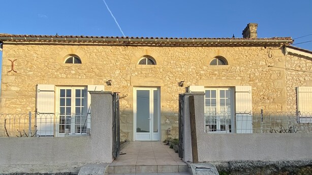 A stone building with a central door and two side doors, surrounded by a metal fence and a small garden area. - Maison Traditionnelle en Campagne (Saint-Quentin-de-Caplong)
