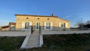 A two-story stone building with a central entrance, a small staircase, and a fenced yard. - Maison Traditionnelle en Campagne (Saint-Quentin-de-Caplong)