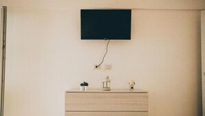 Une chambre dotée d’un téléviseur à écran plat fixé au mur, d’une commode en bois avec des tiroirs et d’une petite plante posée sur la commode.