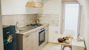 Une cuisine compacte équipée d’une cuisinière, d’un four et d’un évier, une table à manger avec des aliments pour le petit-déjeuner, et une vue sur l’extérieur à travers une porte en arc de cercle.