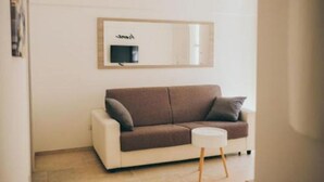 Une pièce moderne avec un canapé blanc, une petite table d’appoint ronde et un miroir fixé au mur.