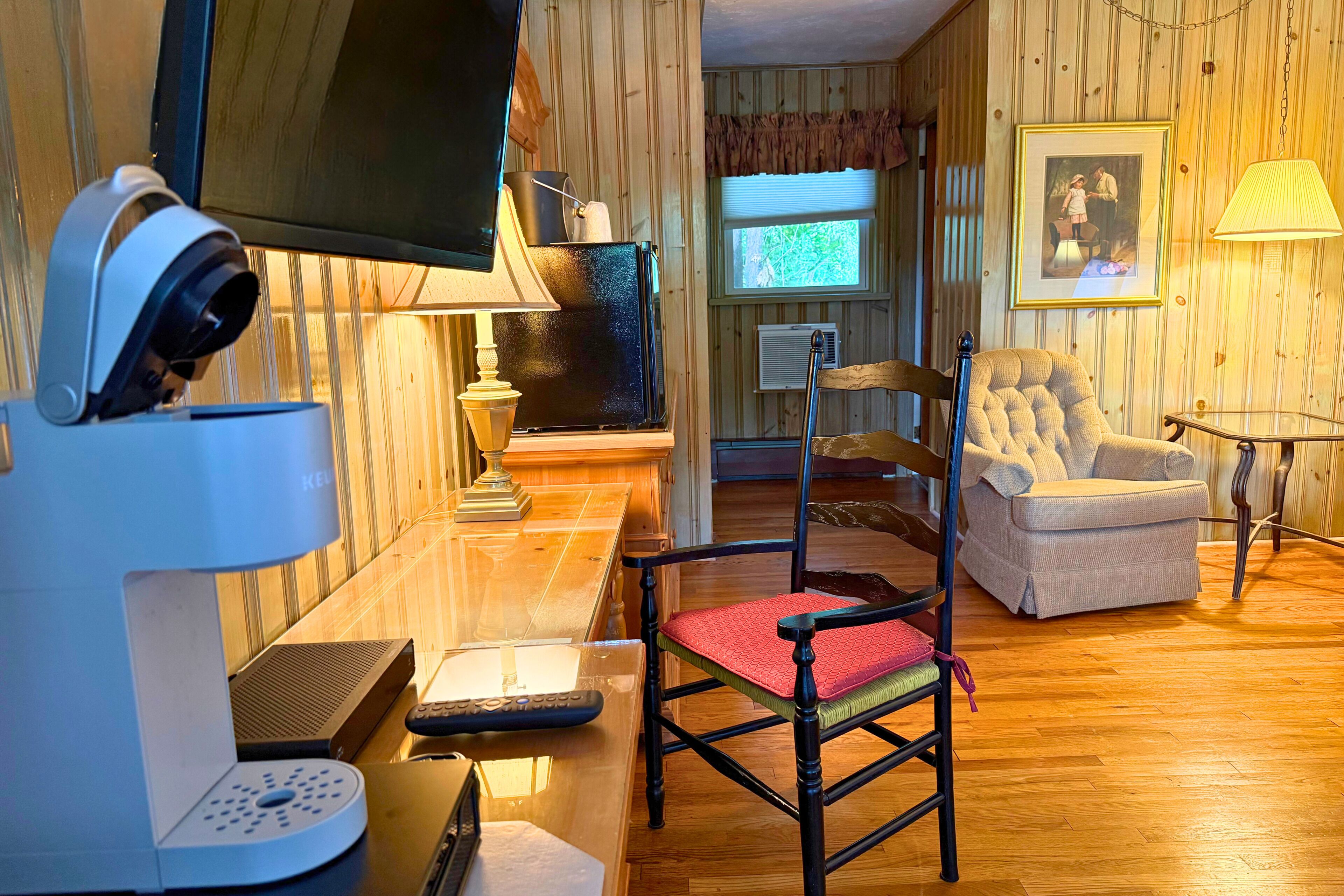 Une pièce comprenant une télévision, un bureau avec un ordinateur, une chaise, une lampe et une fenêtre avec des stores.