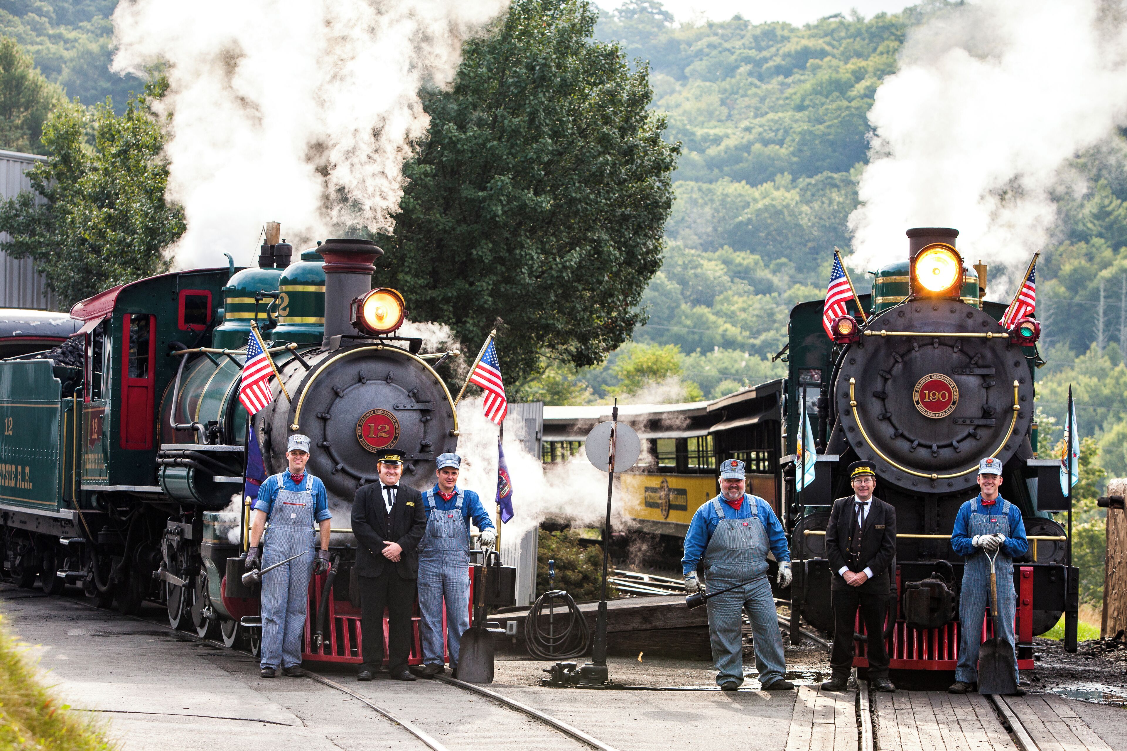 A steam locomotive with American flags, surrounded by workers in blue overalls.