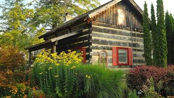 A rustic log cabin with a porch, surrounded by a garden with various plants and flowers.