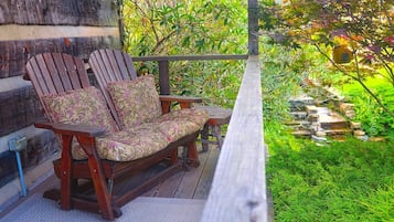 A wooden deck with a bench and a table, surrounded by lush greenery and a small waterfall.