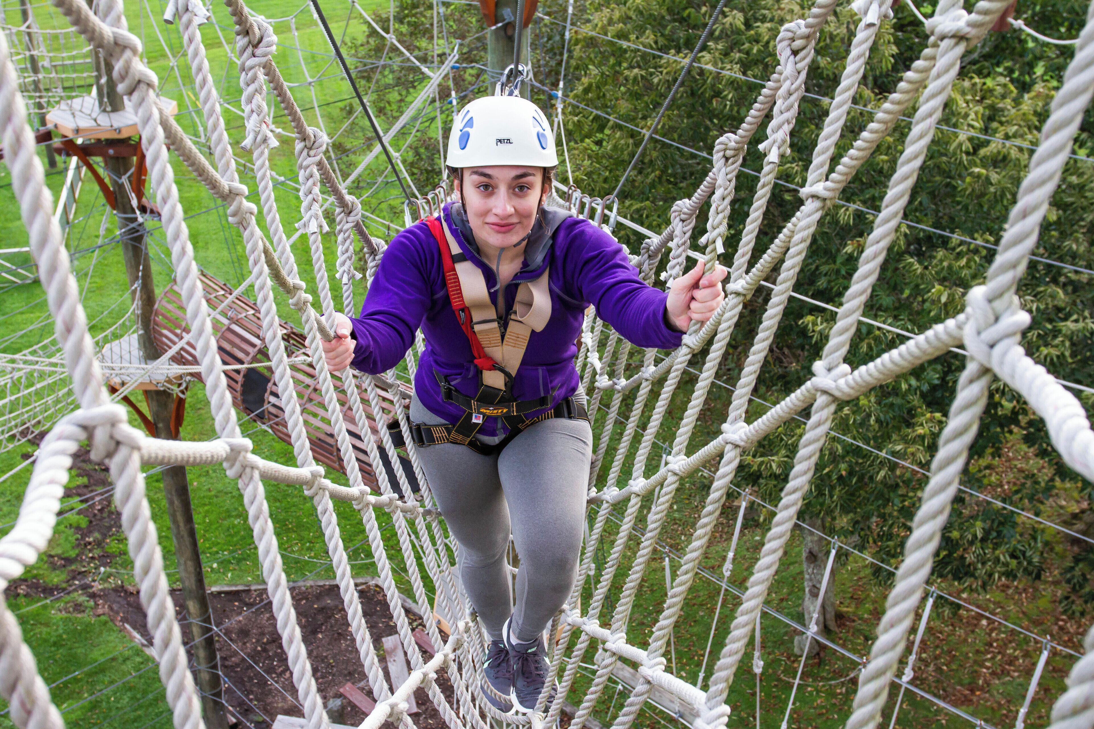 A person navigating a rope bridge with safety harnesses and a helmet.