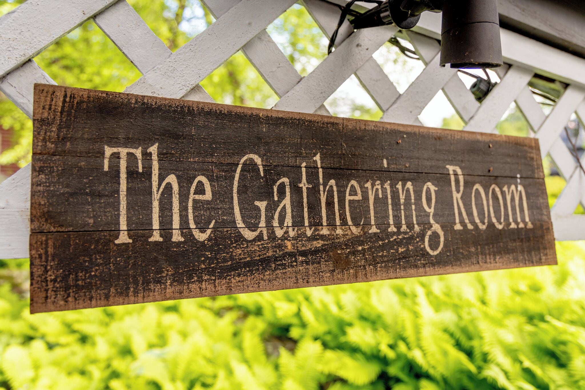 A wooden sign with the text "The Gathering Room" mounted on a white lattice structure.