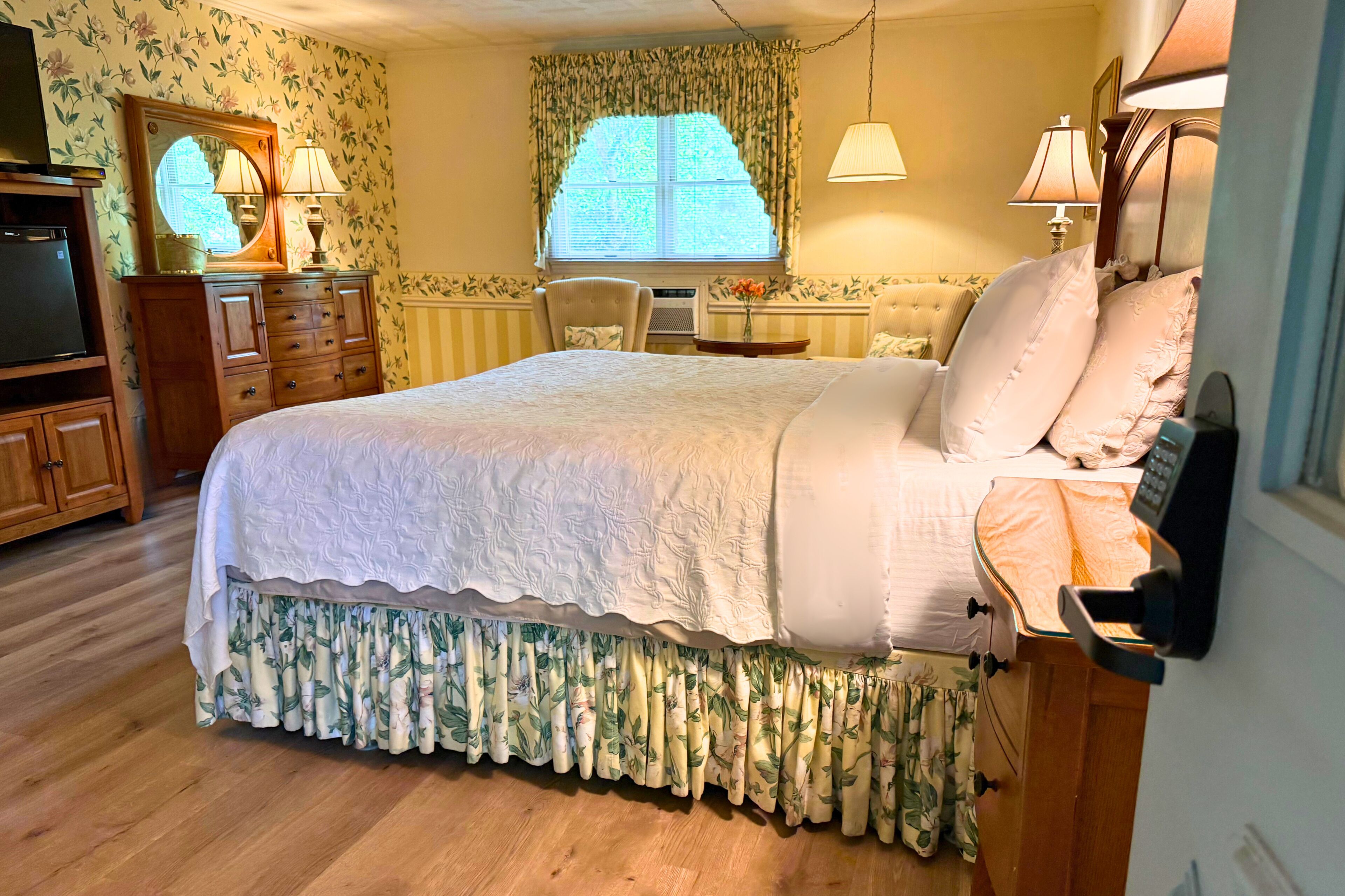 A bedroom with a bed, dresser, vanity, and a window with curtains.