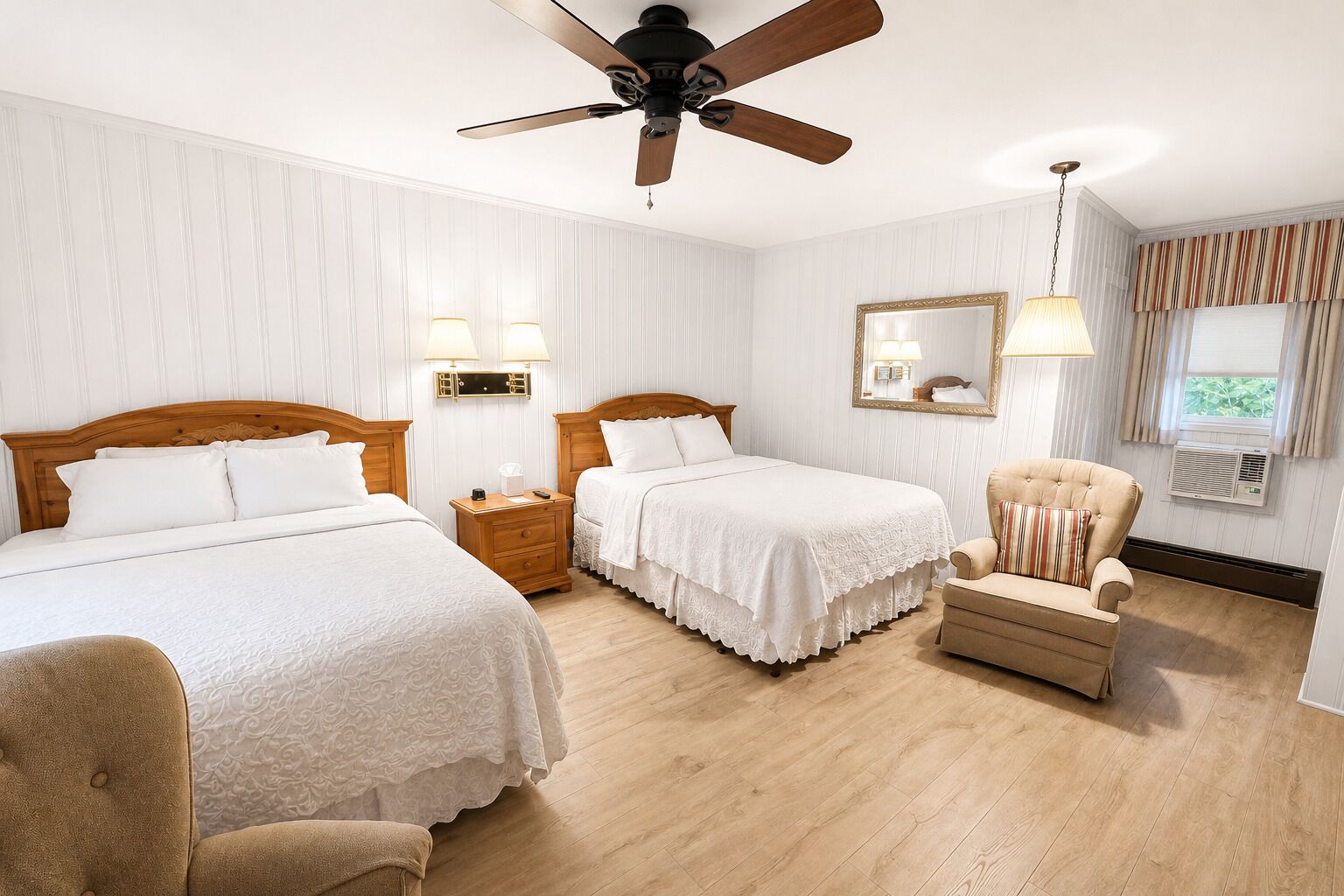 A hotel room with two beds, a ceiling fan, bedside lamps, a chair, a mirror, and a window with curtains.