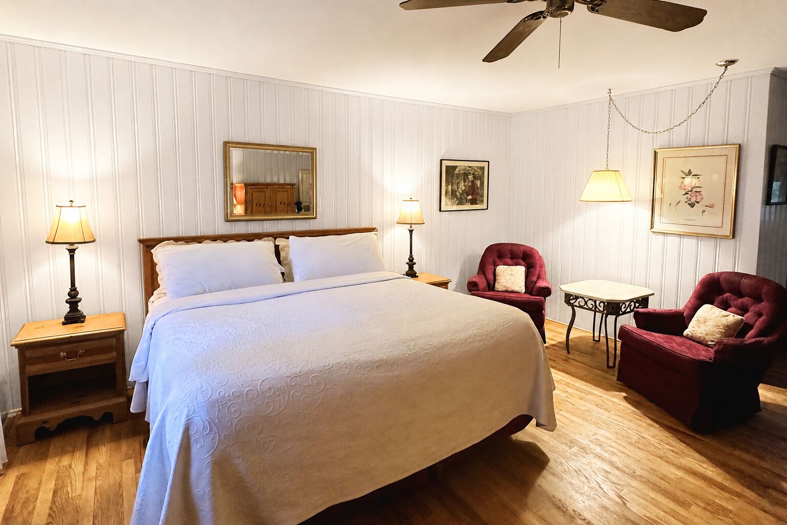 Un dormitorio con una cama grande, dos mesitas de noche, una silla, una mesa y un ventilador de techo.