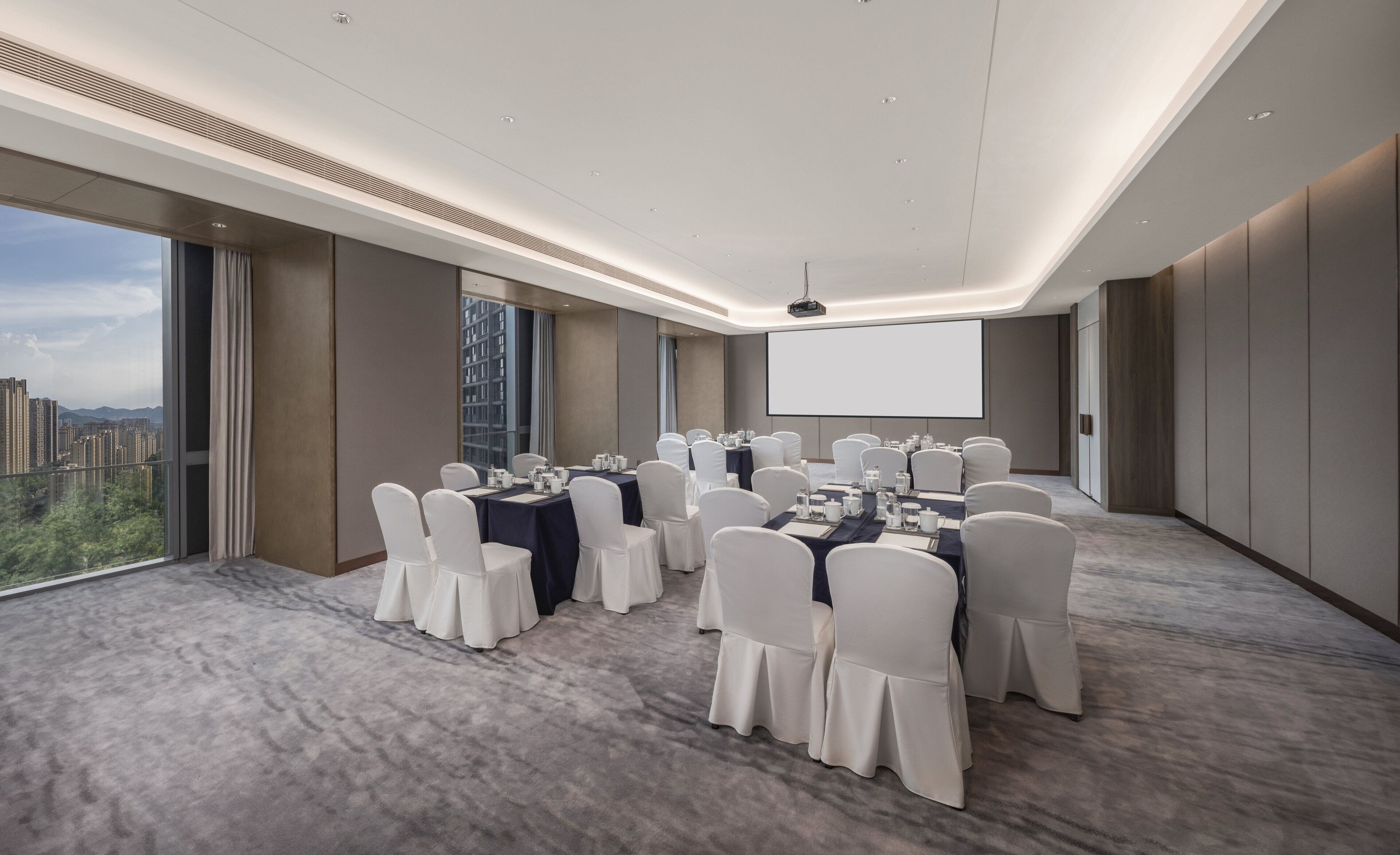 Un salón de conferencias con mesas redondas, sillas blancas y una pantalla grande.