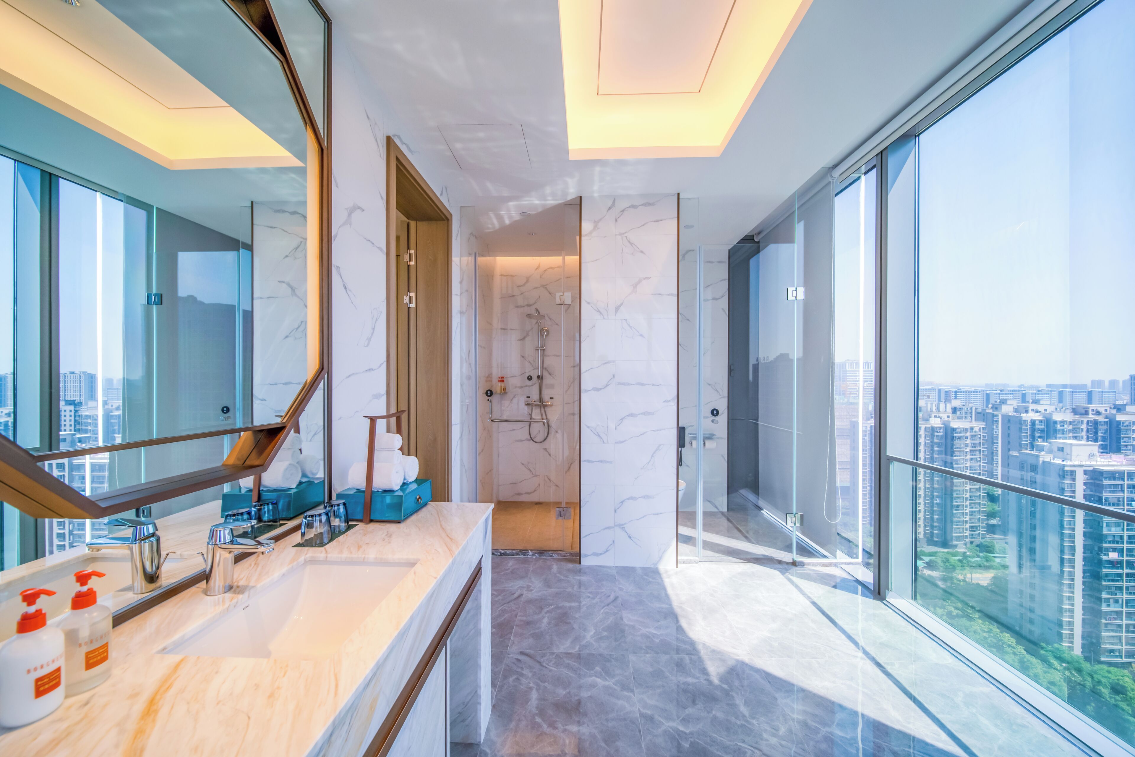 A modern bathroom with a marble vanity, a glass shower enclosure, and a city view.