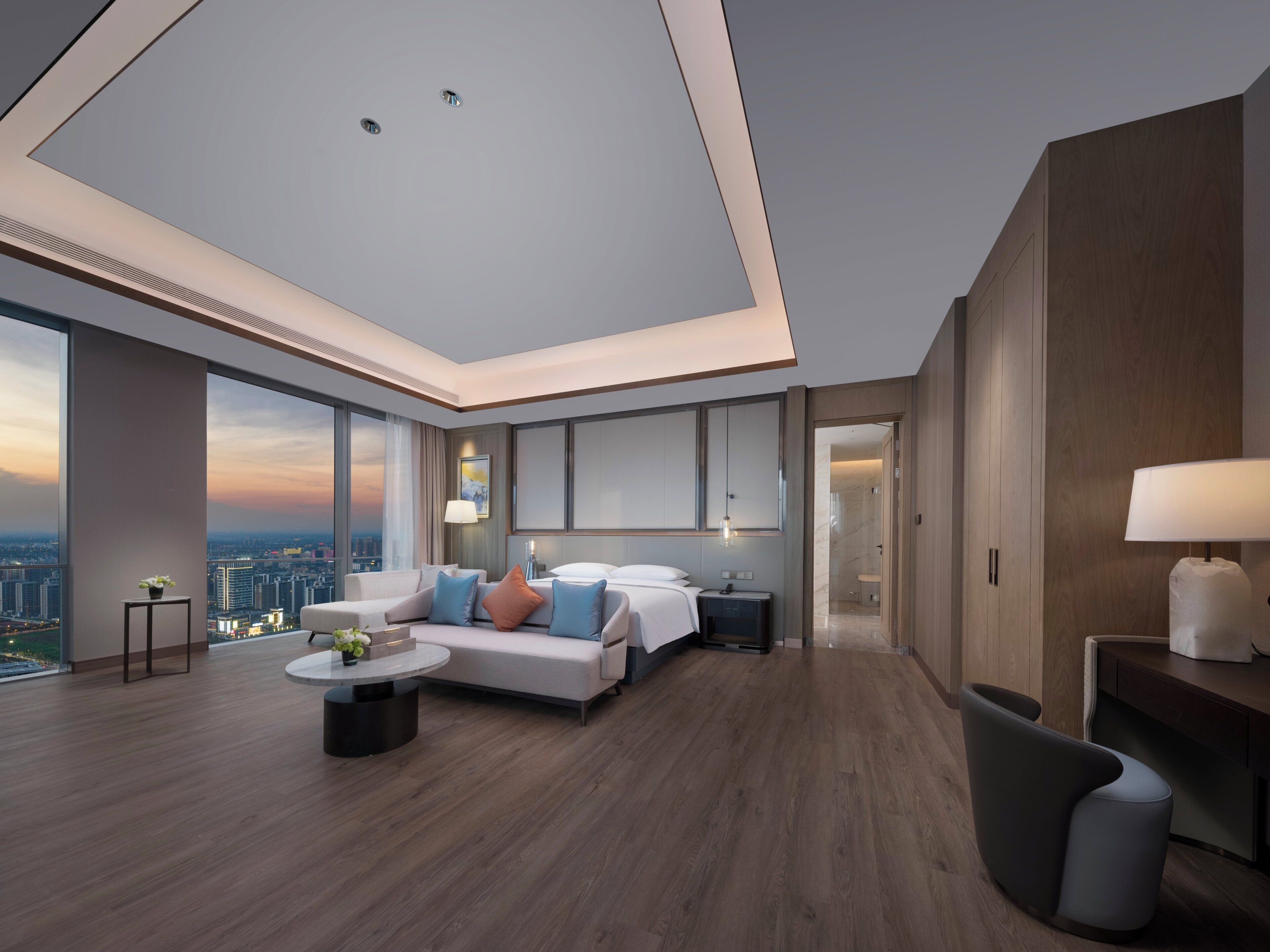 A modern hotel room with a large bed, a seating area with a coffee table, and a view of the city.