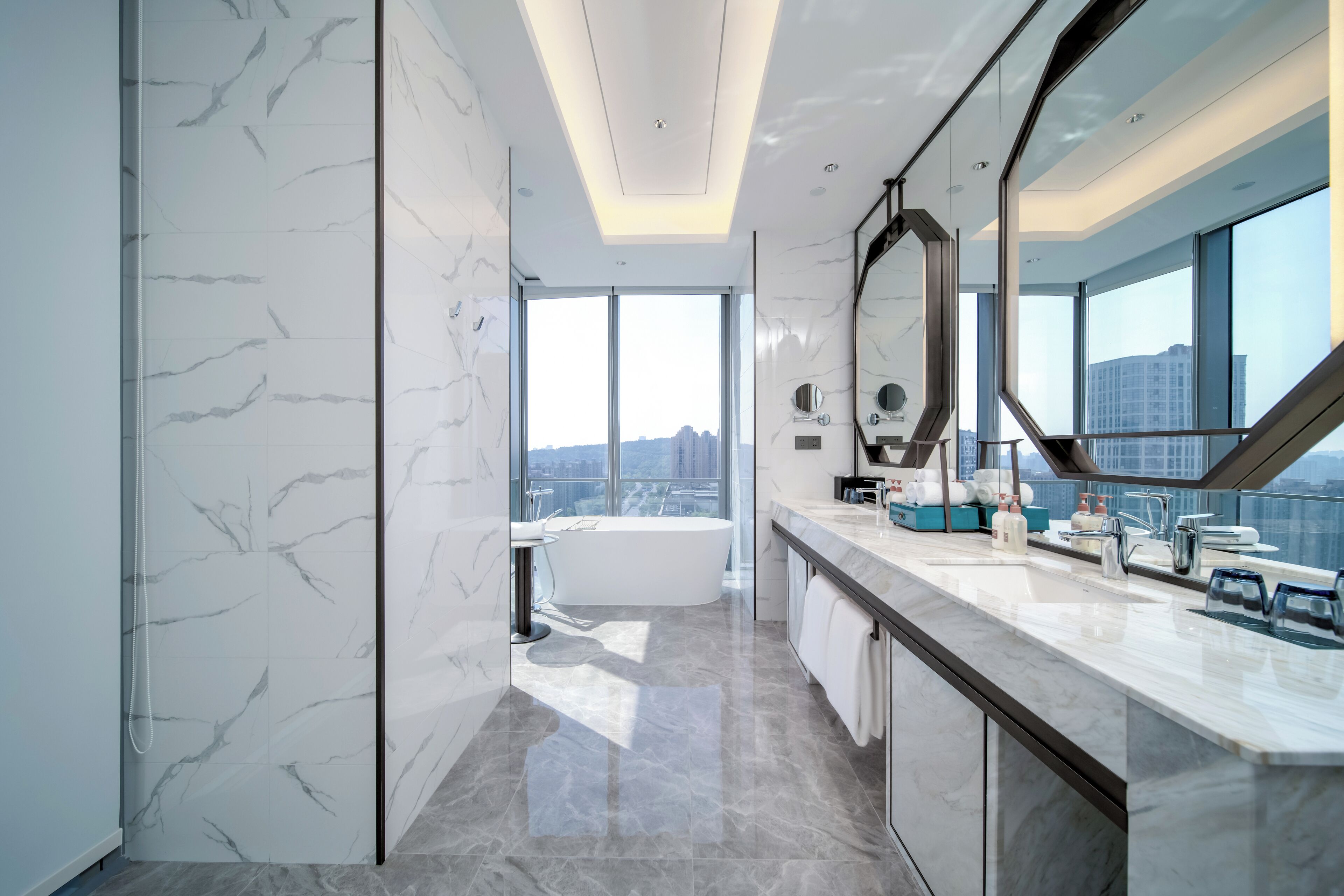 A modern bathroom with a large bathtub, a vanity with a mirror, and a view of the city.