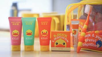 Una colección de productos de tocador de la marca B. Duck, incluyendo loción corporal, jabón de ducha, champú y pasta de dientes, sobre una superficie reflectante.