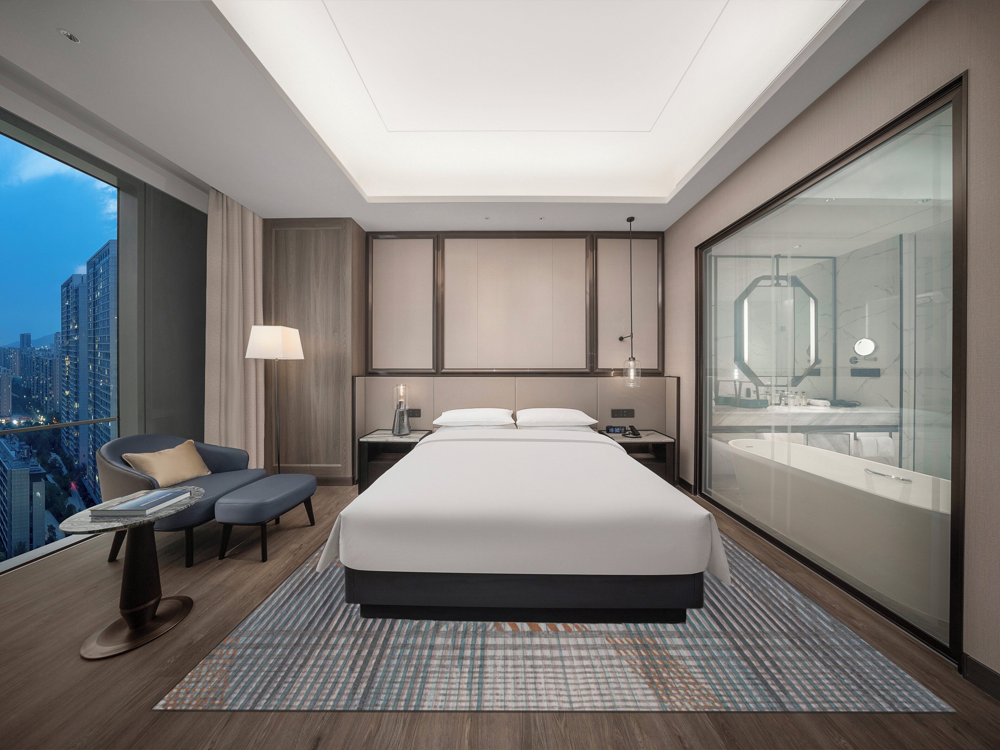 Une chambre d’hôtel moderne dotée d’un grand lit, d’un bureau, d’une chaise, d’une table de chevet et d’une grande fenêtre donnant sur la ville.