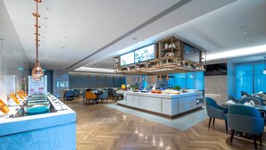 Eine moderne Hotellobby mit einer Marmor-Rezeption, einer zentralen Insellounge und einer hohen Decke mit eingelassener Beleuchtung.