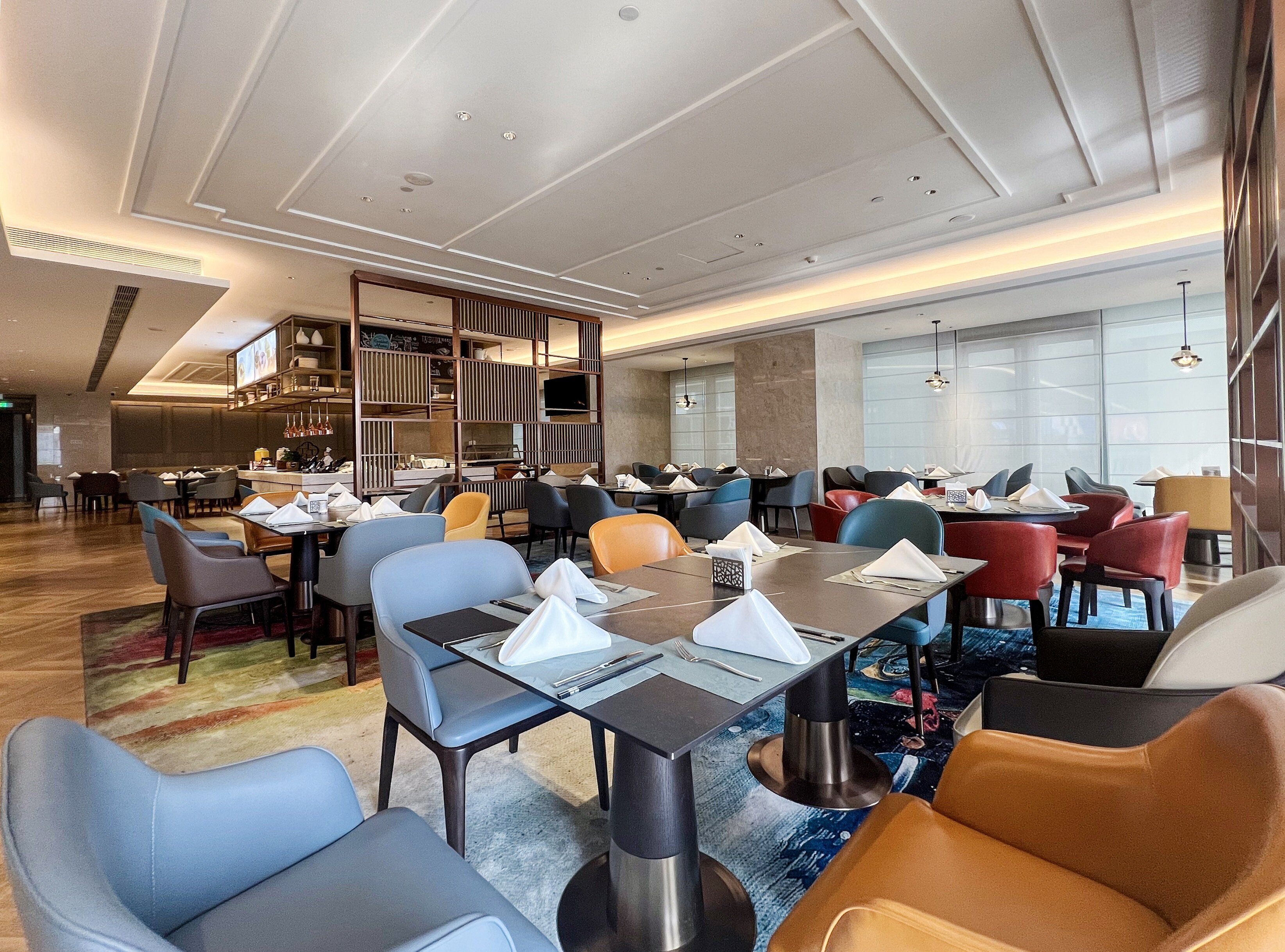 Un comedor moderno de hotel con varias mesas y sillas, una pantalla grande y una zona de bar.