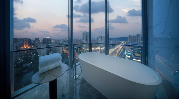 Ein modernes Badezimmer mit freistehender Badewanne, einem Handtuchhalter und einem großen Fenster mit Blick auf die Stadt.
