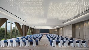 Ein Konferenzraum mit Tischen, weißen Stühlen und einer Decke mit hängenden Leuchten.