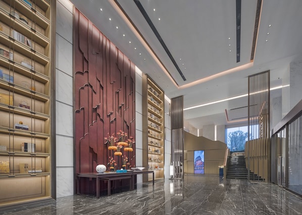 A modern lobby with a marble floor, bookshelves, a decorative wall, and a staircase.