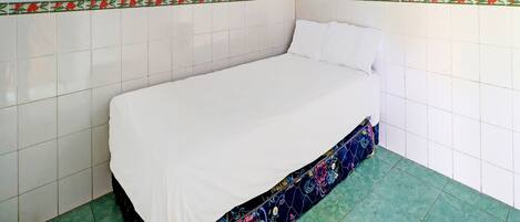 A single-bed room with white bedding, a decorative border on the wall, and a small framed picture above the bed.