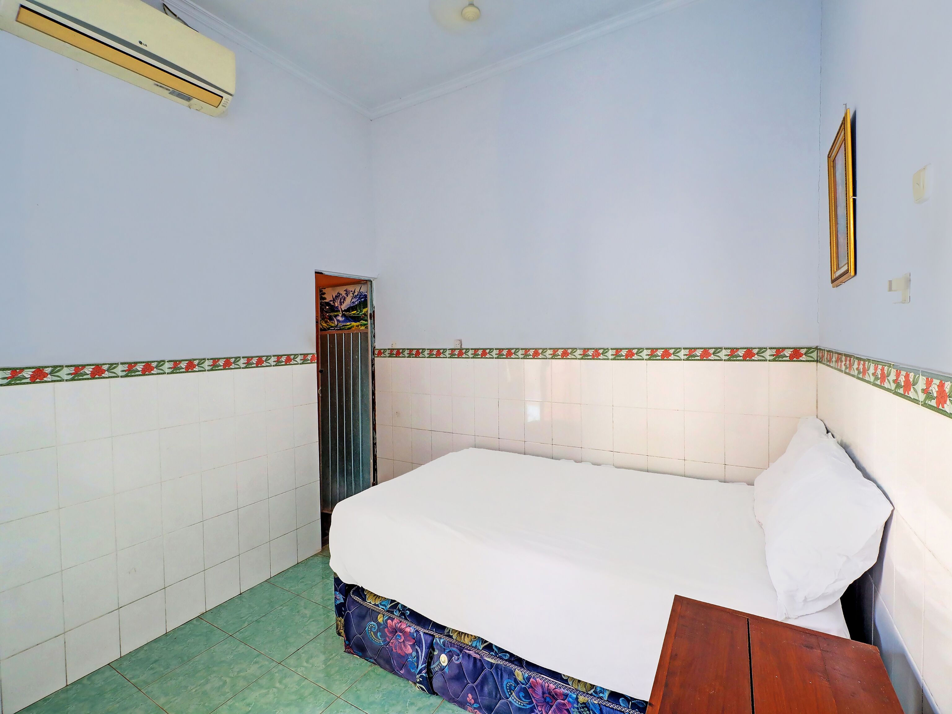 A small, clean room with a bed, a wooden table, and a door leading to another room.